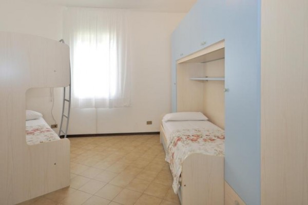 Izba s poschodovou a samostatnou posteľou, svetlým nábytkom a oknom so záclonou.