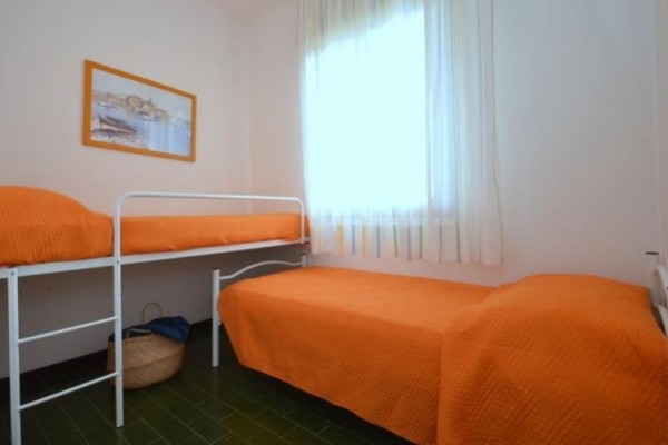Izba s dvoma lôžkami a oranžovými prikrývkami, s obrazom na stene a košom pod posteľou.